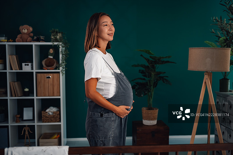 怀孕的女人在婴儿房里抱着肚子，目光投向一旁图片素材
