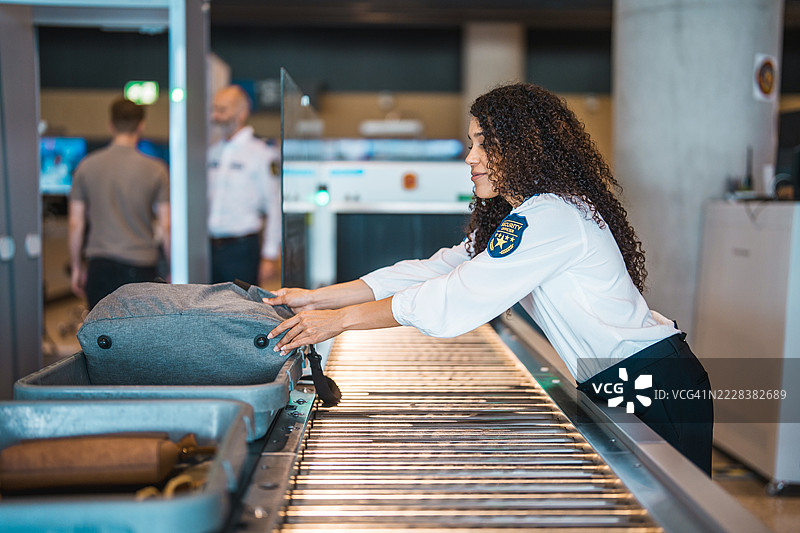 年轻的西班牙裔机场安检员专注而专业地扫描行李图片素材