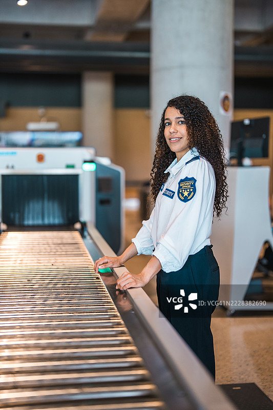 年轻的西班牙裔女性安保人员在机场行李认领区工作，光线自然。图片素材
