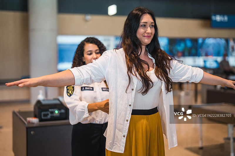 年轻的西班牙裔女性机场安检员在明亮的现代航站楼内为乘客扫描行李图片素材