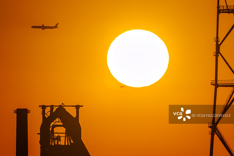 第一缕阳光与一架客机和鸟类的剪影。它即将降落在附近的羽田机场。第一缕阳光越过运河对岸的烟囱和电厂、钢铁厂。图片素材