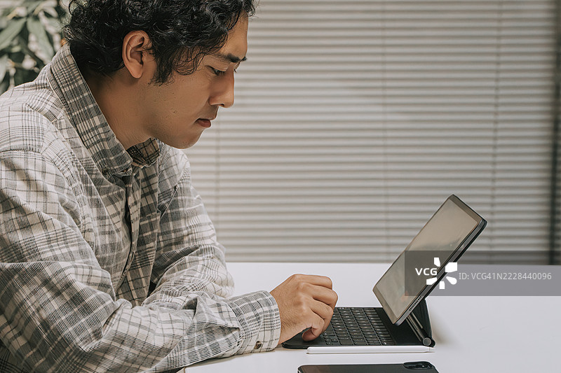 年轻日本男子在办公桌上使用带键盘的平板电脑图片素材