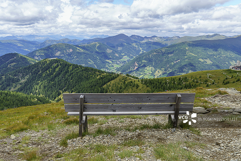 木制长椅提供了在多云天空下的广阔山脉全景,地点:奥地利卡林西亚州的巴德克莱因基希姆。图片素材