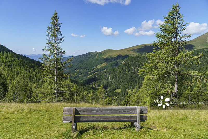 位于克林基希姆，卡林西亚，阿尔卑斯山，奥地利的空地边缘的木长椅，俯瞰着森林山谷。图片素材