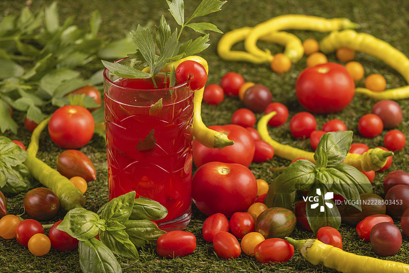 一杯番茄汁周围环绕着番茄、辣椒和草药，放在草地上图片素材