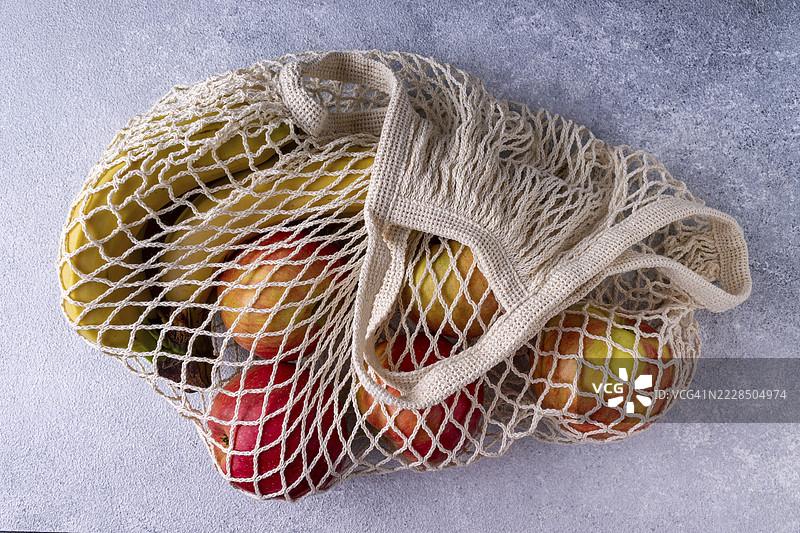 用环保材料制成的绳子袋，里面有香蕉和苹果，背景是灰色的灰泥。图片素材