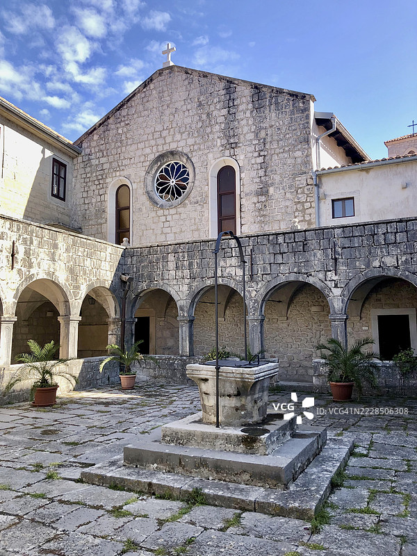 一个宁静的修道院庭院，中央有喷泉，古老的石墙，位于克罗地亚克尔克岛附近的普纳特岛上的科什柳恩岛修道院。图片素材