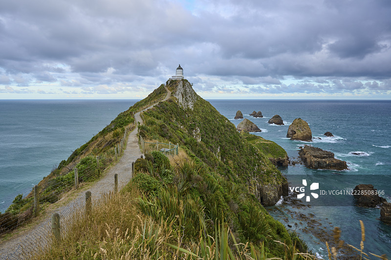 一条小路沿着绿色海岸延伸至灯塔,海景迷人,夏季,纳格特角灯塔,阿胡里平原,奥塔哥,南岛,新西兰图片素材