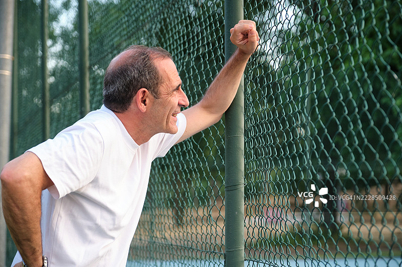 成熟的网球运动员在比赛后休息，靠在围栏上图片素材