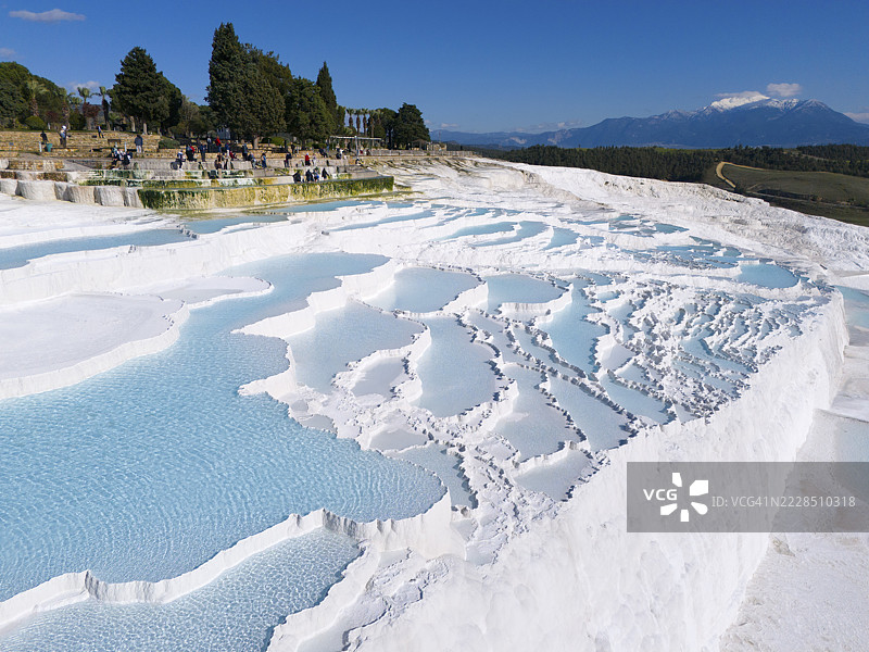 石灰岩梯田的景观,碧蓝的水域被树木和游客环绕,鸟瞰图,石灰华梯田,石灰岩梯田,钙华梯田,棉花堡,德尼兹利,联合国教科文组织世界遗产,安纳托利亚,土耳其图片素材