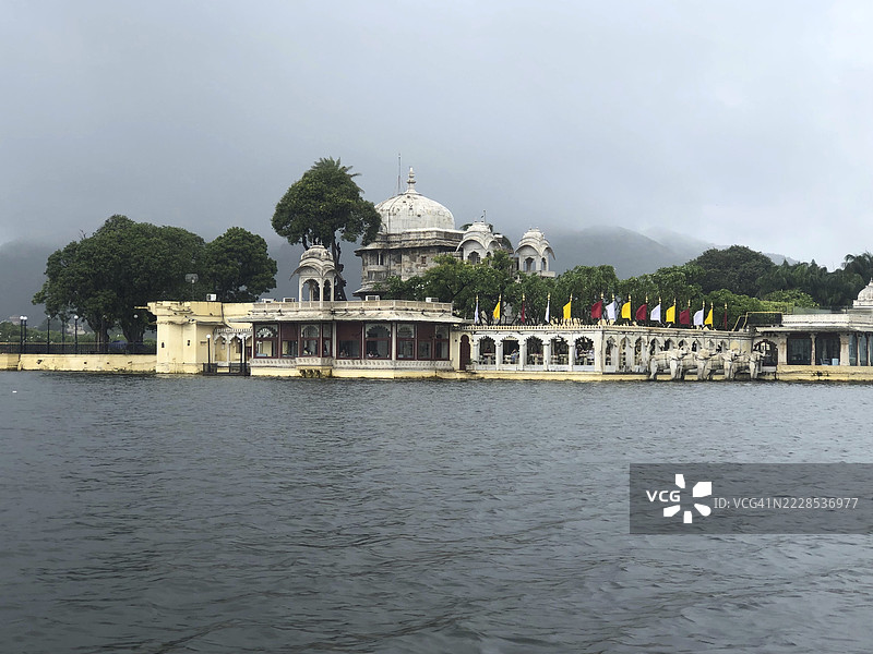 一座宏伟的湖畔宫殿,周围环绕着郁郁葱葱的绿植和壮丽的建筑,皮丘拉湖,乌代浦,拉贾斯坦邦,印度图片素材