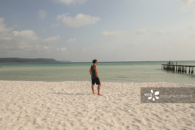 一位男士站在沙滩上，眺望着柬埔寨西哈努克省戈公岛的平静海面图片素材
