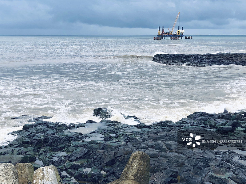 孟买，马哈拉施特拉邦，班德拉海滩，岩石海岸线，背景有桥梁建设平台和多云的天空图片素材