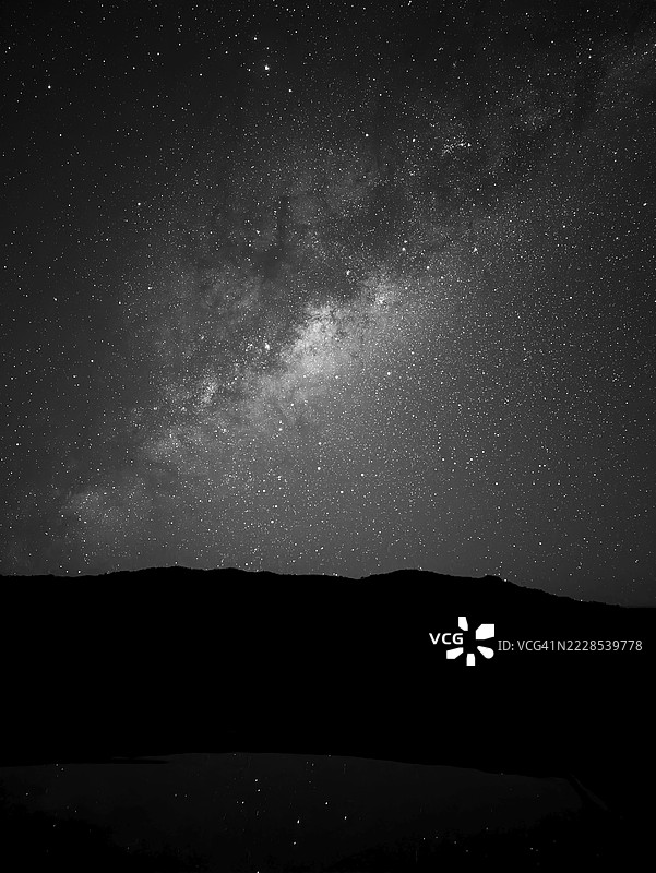 星空璀璨，银河高悬于黑暗的剪影景观之上。法属留尼旺岛。图片素材