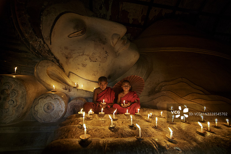 两位身穿传统袈裟的佛教僧侣坐在佛像前，周围点缀着蜡烛，正在祈祷，缅甸图片素材