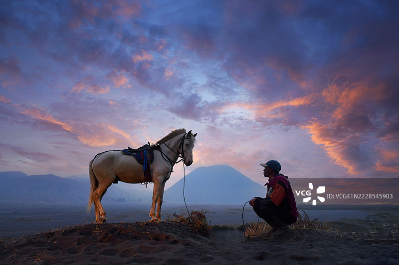 男子蹲在他的马旁，位于印度尼西亚东爪哇的布罗莫腾格尔塞梅鲁国家公园图片素材
