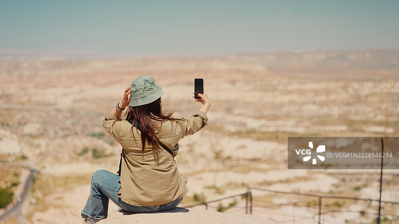 女性旅行者坐在岩石上，拍摄山间风景的照片和视频图片素材