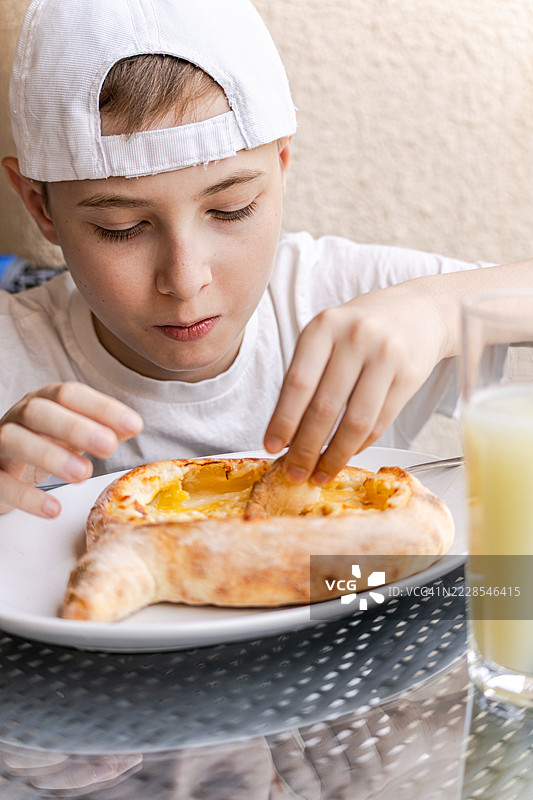 戴着棒球帽的少年坐在街头咖啡馆里，享用传统的阿贾里哈奇普里和拉吉泽水。图片素材