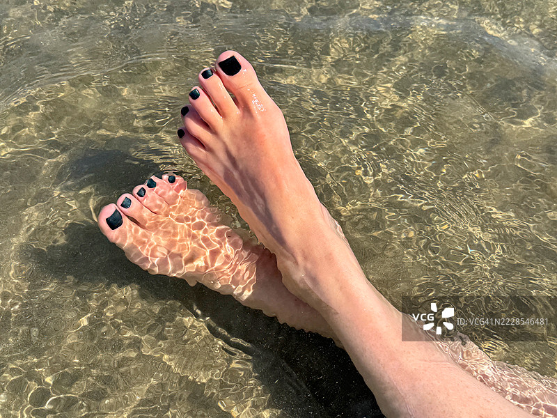 女人的脚在法国普罗旺斯-阿尔卑斯-蓝色海岸地区的圣玛丽德拉梅尔沙滩的浅水中特写。图片素材