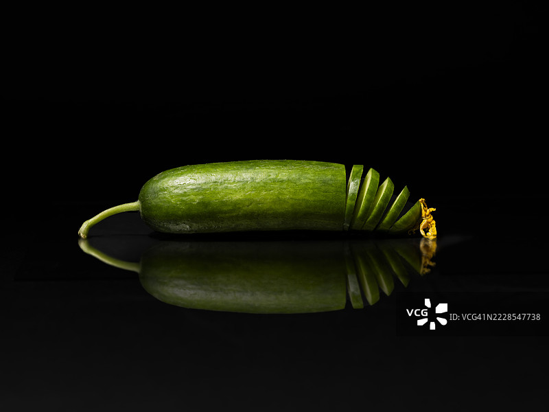 半个切片黄瓜的特写与黑色背景上的倒影图片素材