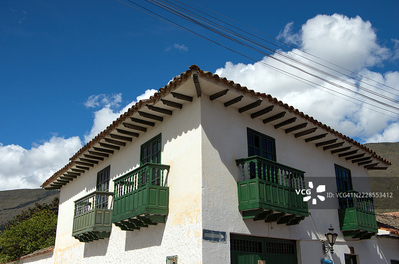 两层白washed石头和灰泥的殖民时代建筑，配有红陶屋顶、窗框窗户和四个小木阳台。图片素材