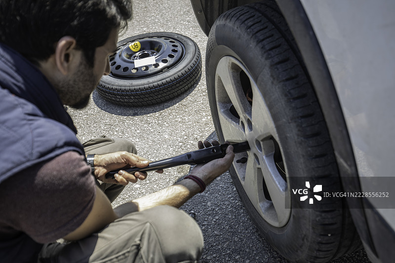 男子在路边故障时用轮胎扳手更换轮胎图片素材
