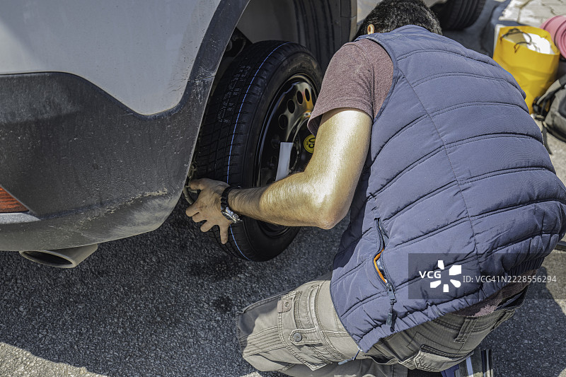 男子在路边更换平胎，使用备用轮胎，因汽车故障而停靠。图片素材