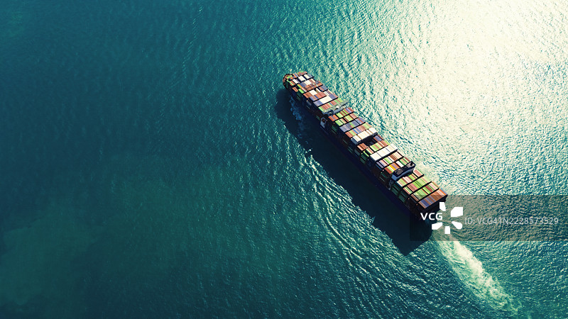 航拍视角的集装箱货船，满载集装箱，从商业港口的码头出发，适用于商业物流、进出口、航运或货物运输。图片素材