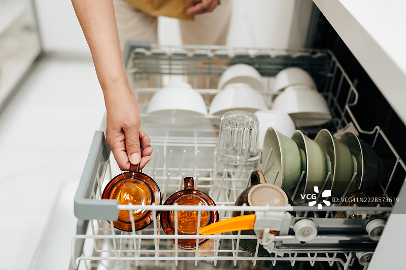亚洲老年女性的手特写，将脏玻璃杯放入洗碗机。图片素材