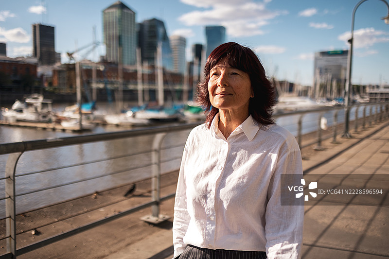 女人在水边散步，背景是码头和城市摩天大楼图片素材