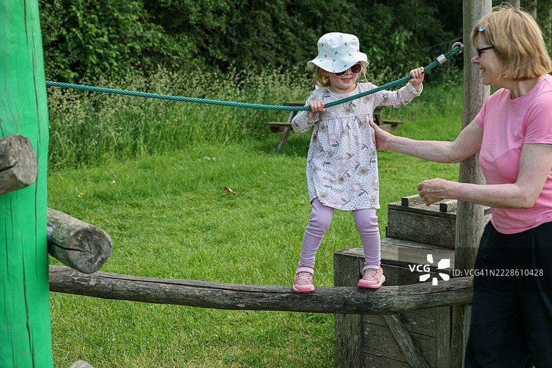 祖母帮助她紧张的四岁孙女穿越游乐场的平衡障碍课程图片素材