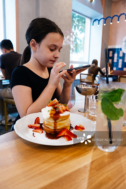 女孩在餐厅里吃煎饼。孩子们的甜美早餐。图片素材