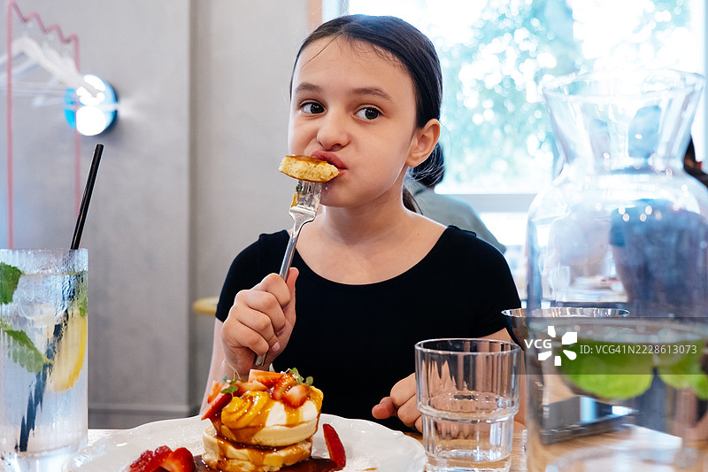 女孩在餐厅里吃煎饼。孩子们的甜美早餐。图片素材