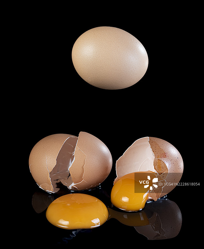 三个鸡蛋掉落并破裂，蛋黄洒落在黑色背景上。图片素材