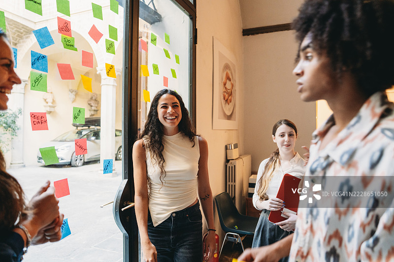 年轻女商人走进办公室，与同事打招呼图片素材
