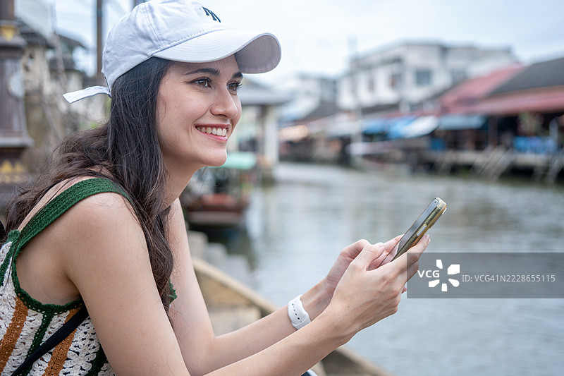 年轻女性游客在泰国的水上市场乘坐木船，品尝当地街头美食，享受东南亚之旅。图片素材