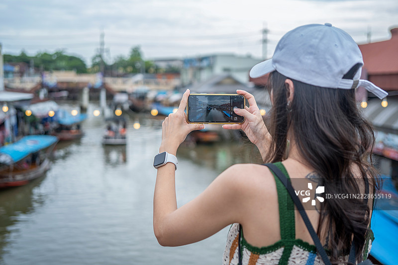 年轻女性游客在泰国的水上市场乘坐木船，品尝当地街头美食，享受东南亚之旅。图片素材