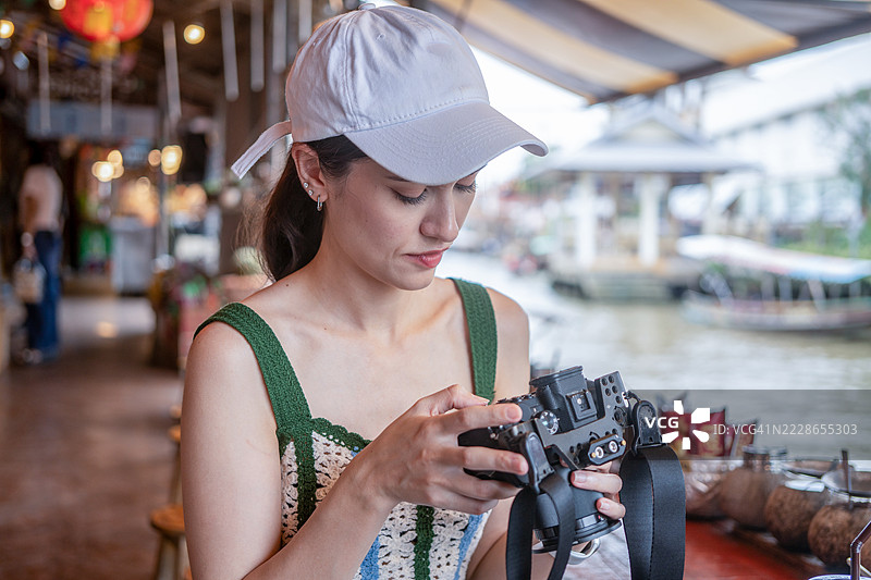 年轻女性在传统船上拍摄漂浮市场的照片。旅行与科技概念。图片素材