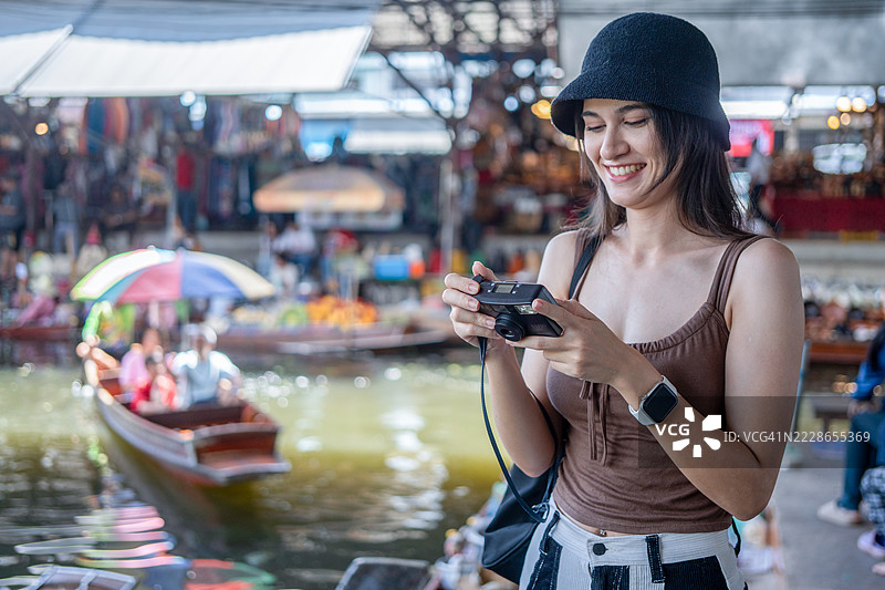 年轻女性游客在泰国的水上市场乘坐木船，品尝当地街头美食，享受东南亚之旅。图片素材