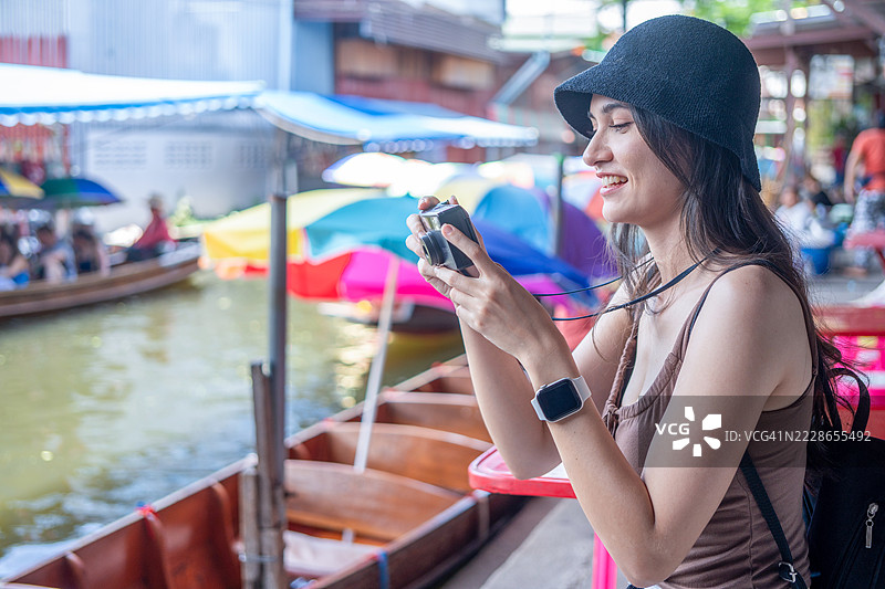 年轻女性游客在泰国的水上市场乘坐木船，品尝当地街头美食，享受东南亚之旅。图片素材