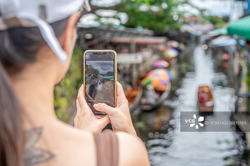 年轻女性游客在泰国的水上市场乘坐木船，品尝当地街头美食，享受东南亚之旅。图片素材