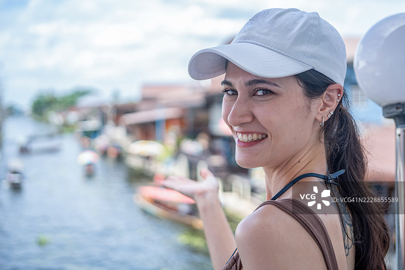 年轻女性游客在泰国的水上市场乘坐木船，品尝当地街头美食，享受东南亚之旅。图片素材