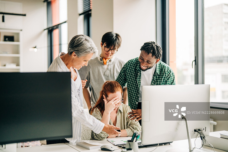 一群年轻的专业人士和他们的资深同事围坐在桌子旁，注视着一位年轻女性，她用双手捂住脸，可能是因为疲惫或兴奋。图片素材