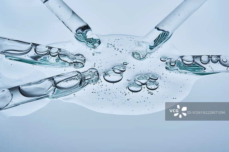 血清从几个移液管流入蓝色背景上的单一纹理中图片素材