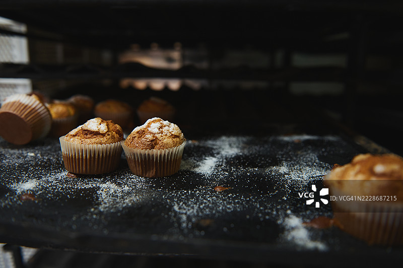 新鲜出炉的松饼放在撒有面粉的托盘上，背景是面包店环境图片素材