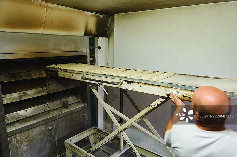 面包师将新鲜整形的面团放入传统烤箱中图片素材