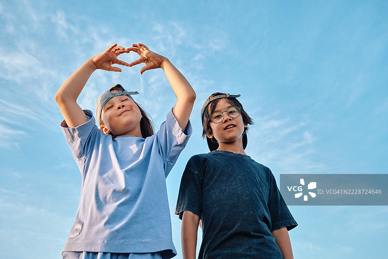 一个男孩和一个女孩在天空背景下对着镜头做鬼脸。图片素材