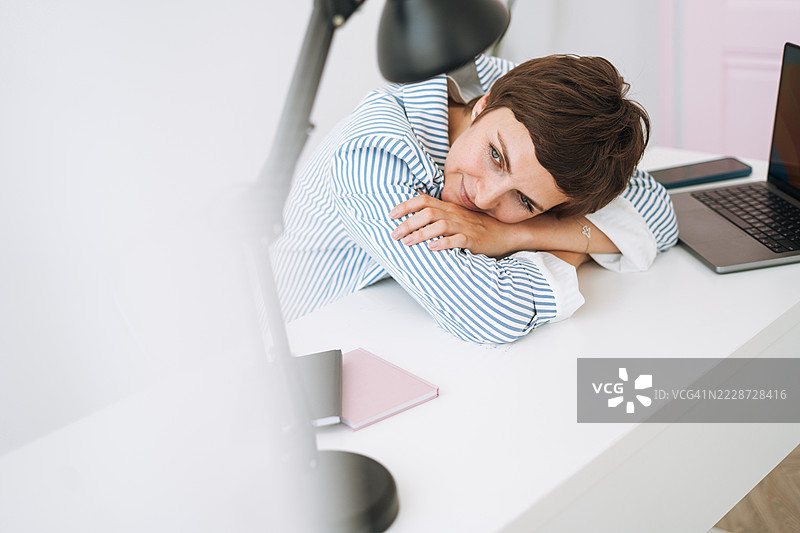 疲惫的女商人在办公室加班，虽然疲惫但专注于笔记本电脑，体现了职场疲劳的概念图片素材
