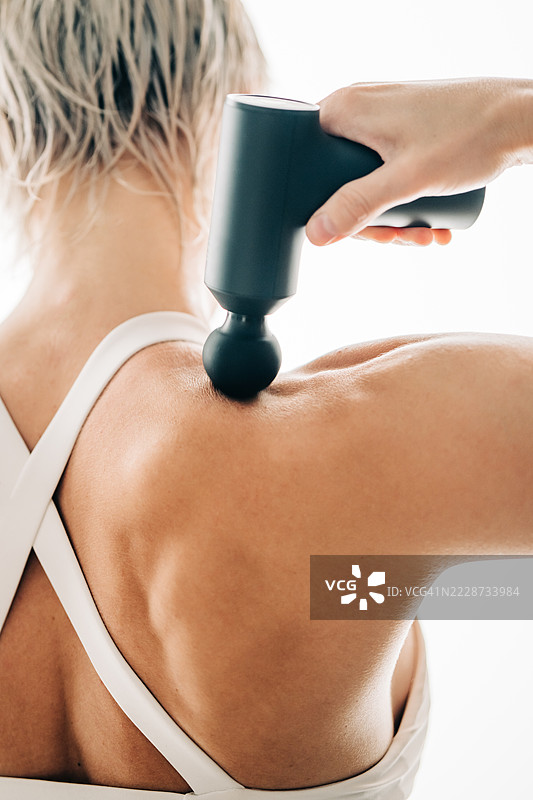 运动后按摩疗法。女人使用冲击按摩器的背面视图。图片素材