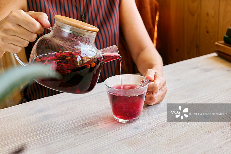 一个无法辨认的女性在家中将洛神花茶倒入玻璃茶杯中图片素材